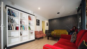 A modern living room with a red sofa, a yellow armchair, and a white bookshelf filled with books. - Enjoy Hostel (Paris)