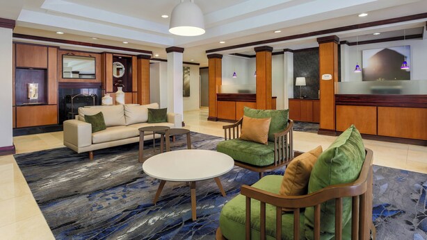 A hotel lobby with a reception desk, seating area with sofas and chairs, a coffee table, and a large mirror. - Fairfield Inn & Suites Mahwah (Mahwah)
