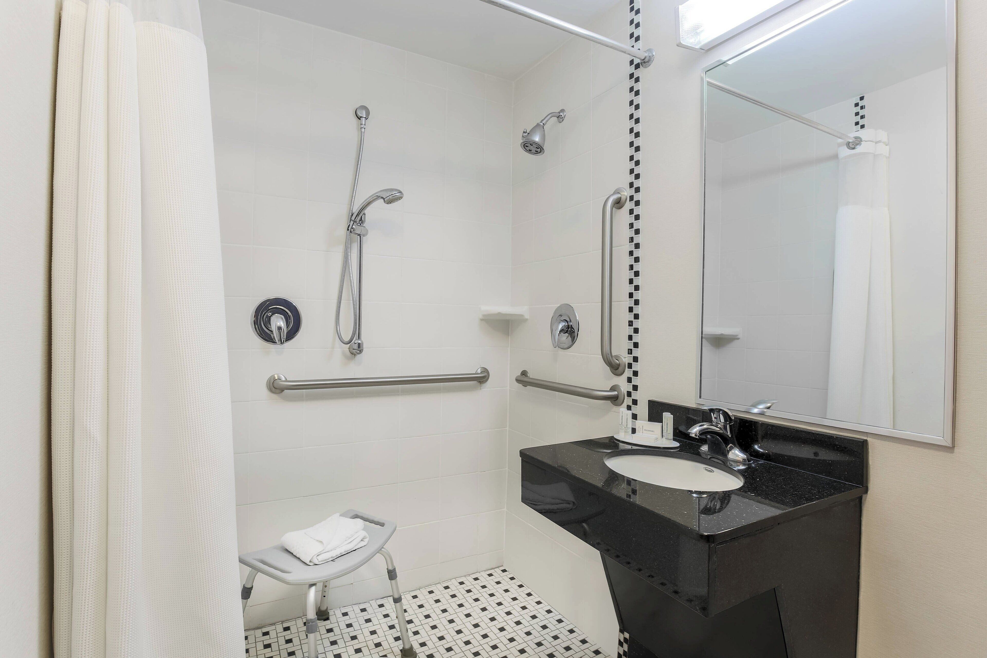 A bathroom with a black sink, white tiles, a handheld showerhead, a handheld showerhead, a towel rack, and a mirror.