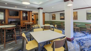 A hotel dining area with multiple tables and chairs, a flat-screen TV mounted on the wall, and artwork on the walls. - Fairfield Inn & Suites Mahwah (Mahwah)