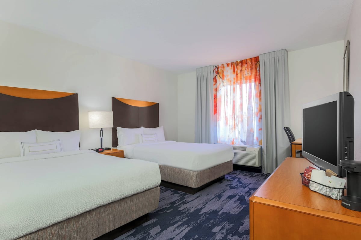 Een hotelkamer met twee bedden, een bureau met een televisie, een lamp en een raam met gordijnen.