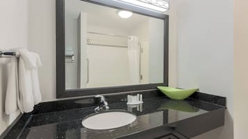 A bathroom with a black countertop, a white sink, a green bowl, and a large mirror with a light above it.