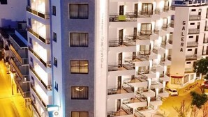 Un hotel de varios pisos con balcones, un letrero vertical en el centro y una calle al frente.