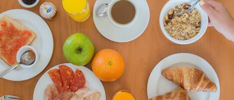 A breakfast table with plates of food, a glass of orange juice, a cup of coffee, and a bowl of cereal.