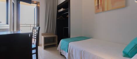 A hotel room with a bed, a desk, a chair, a wardrobe, and a painting on the wall.