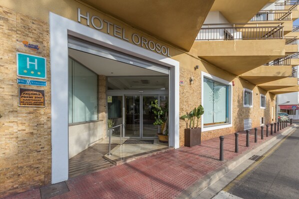 A hotel entrance with a glass door, a sign indicating it is a small, friendly hotel, and a wheelchair-accessible ramp.