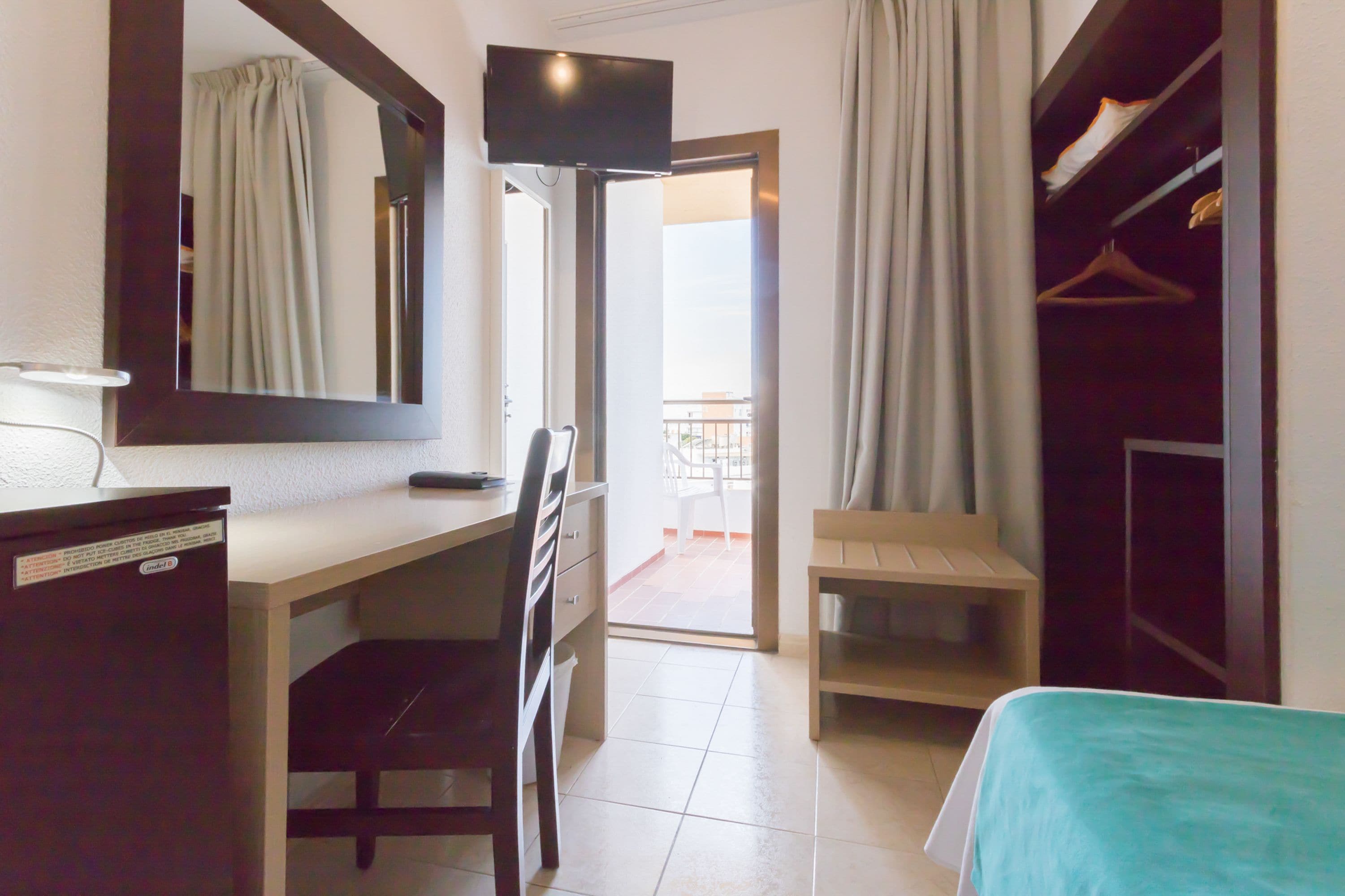 Une chambre d’hôtel équipée d’un bureau, d’une chaise, d’un lit, d’une télévision, d’une armoire et offrant une vue sur le balcon.