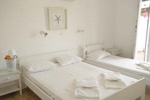 A clean, white room with two single beds, a small bedside table with a lamp, and a framed picture on the wall.