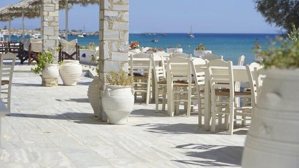A beachside outdoor seating area with white chairs and tables, stone pillars, and potted plants.