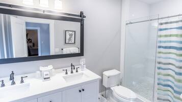 A modern bathroom with a white vanity, a large mirror, a glass shower enclosure, and a striped shower curtain.