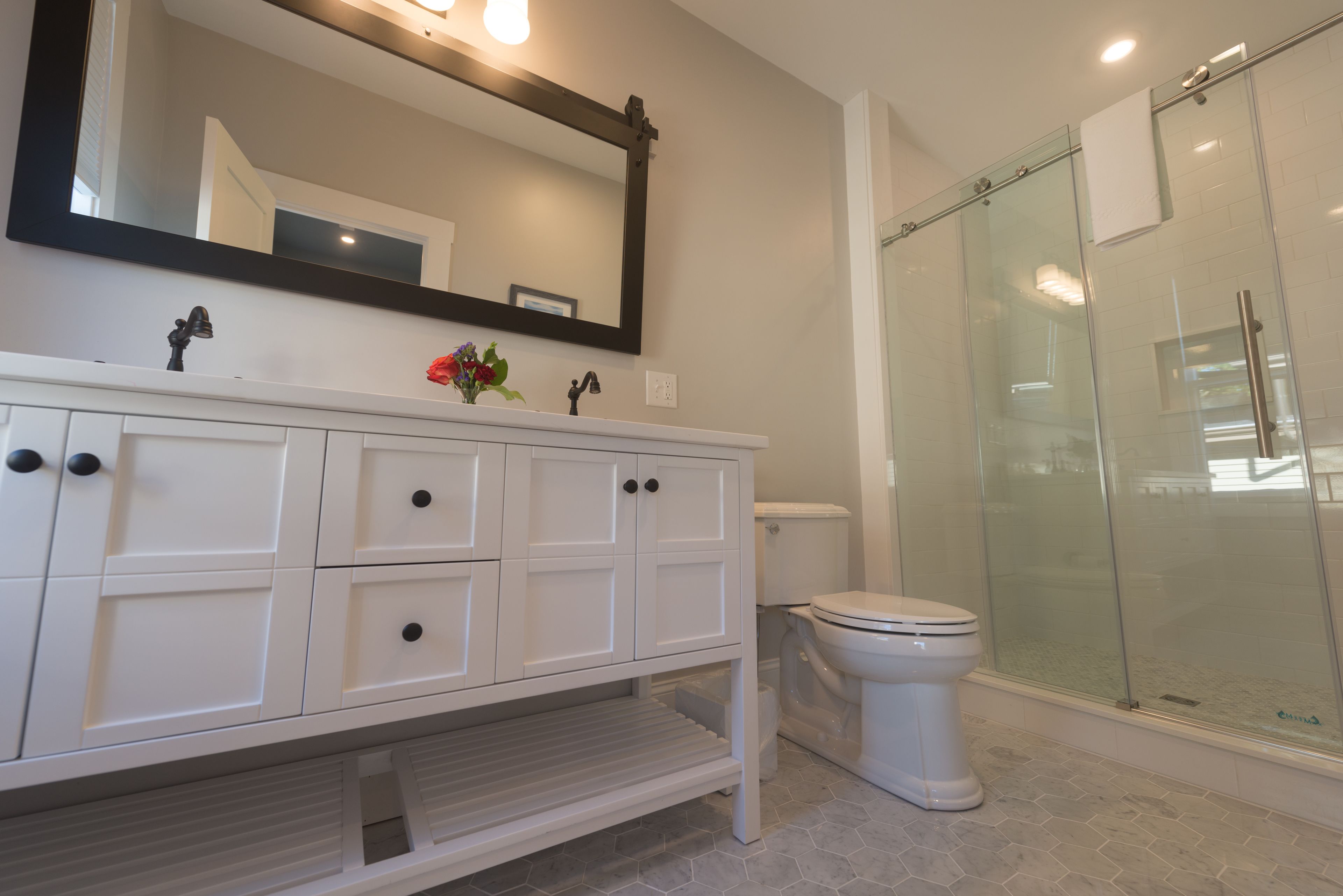 A bathroom with a white vanity, a large mirror, a toilet, and a glass-enclosed shower.