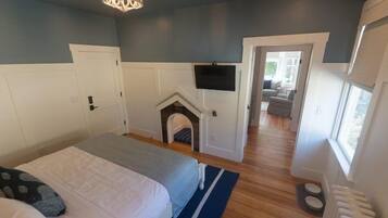 A bedroom with a bed, a fireplace, a TV, and a view of a living area.
