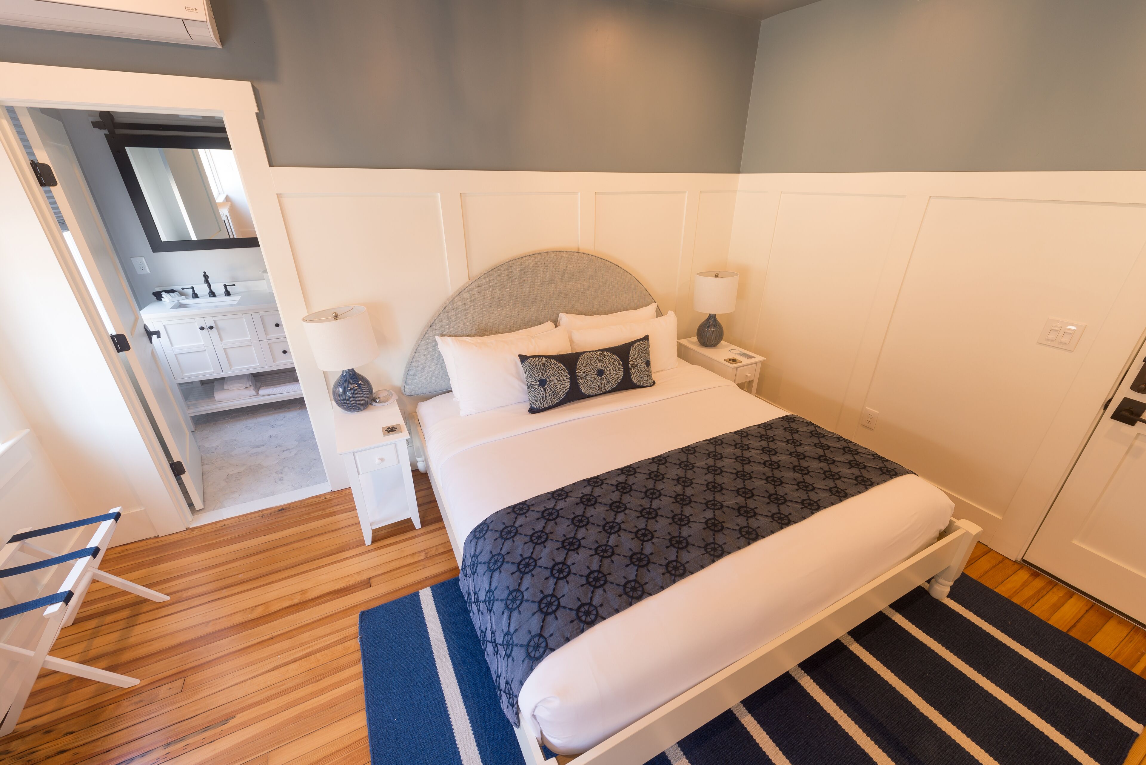 Un dormitorio ordenado con cama, mesitas de noche y un baño visible a través de una puerta abierta.