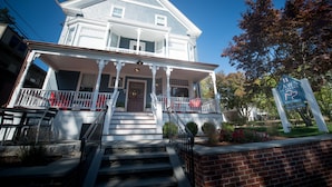 A two-story house with a porch, a brick foundation, and a sign indicating it is a pet-friendly home. - Paws on Pelham (Newport)