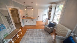 A modern living room with a wooden floor, a large rug, and a seating area with two sofas. - Paws on Pelham (Newport)