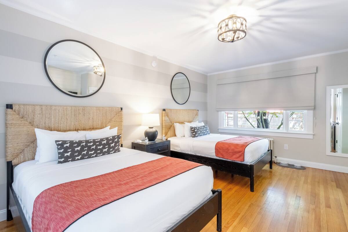 A hotel room with two beds, a large mirror, a chandelier, and a view of the outdoors.
