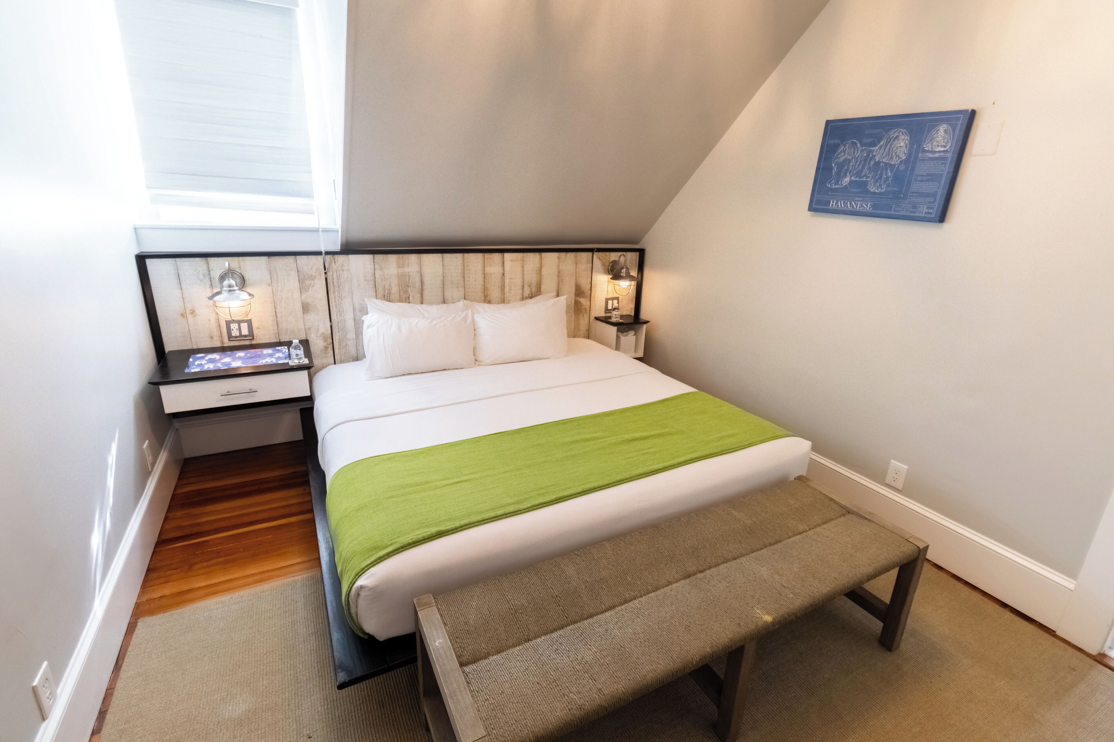 A bedroom with a bed, bedside tables, a bench, and a wall-mounted artwork.