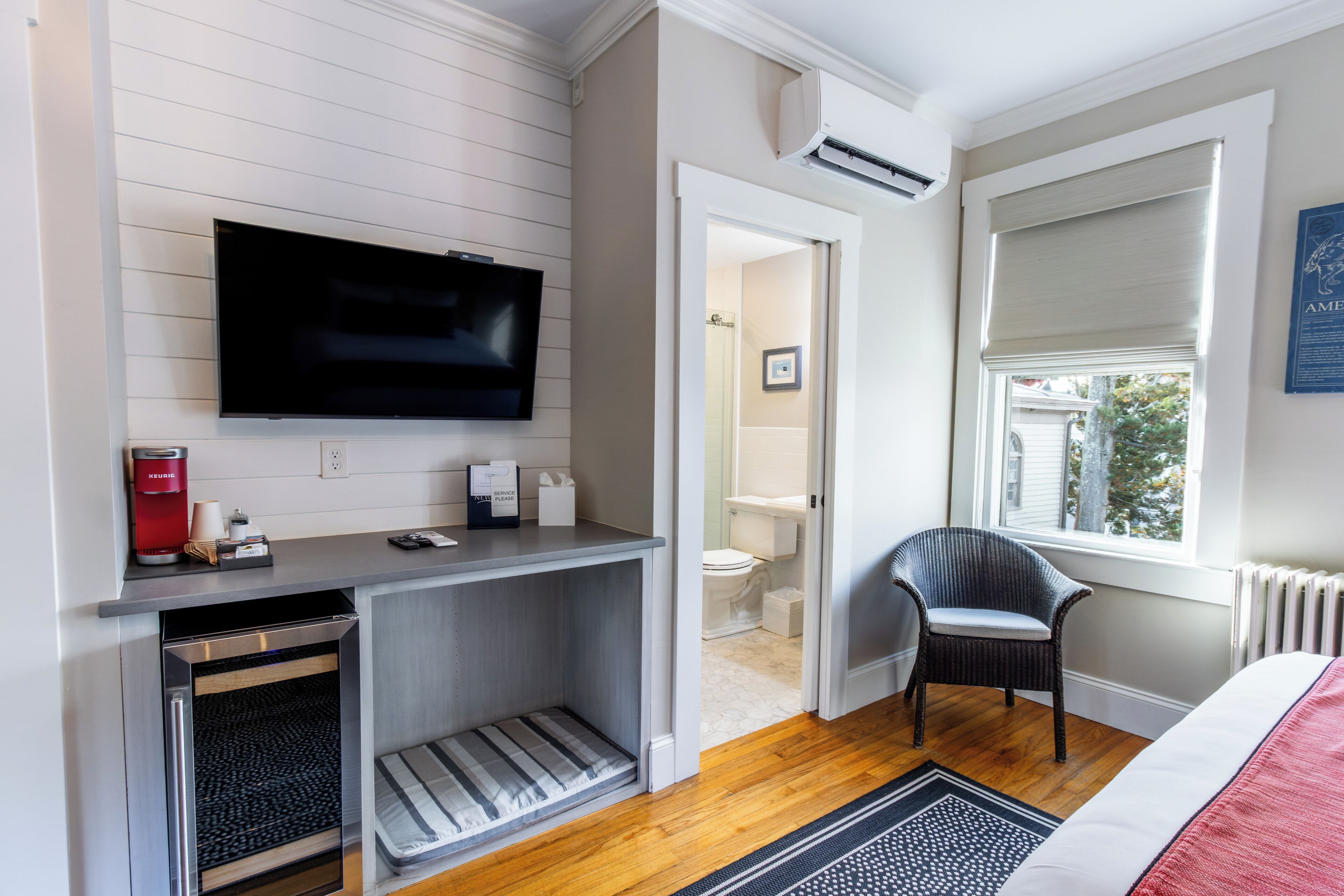 Une chambre d’hôtel compacte dotée d’une télévision à écran plat, d’une kitchenette, d’un plancher en bois, d’une fenêtre avec stores et d’une vue sur l’extérieur.