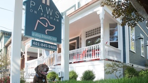 A house with a porch, a dog, and a sign advertising a dog-friendly inn. - Paws on Pelham (Newport)