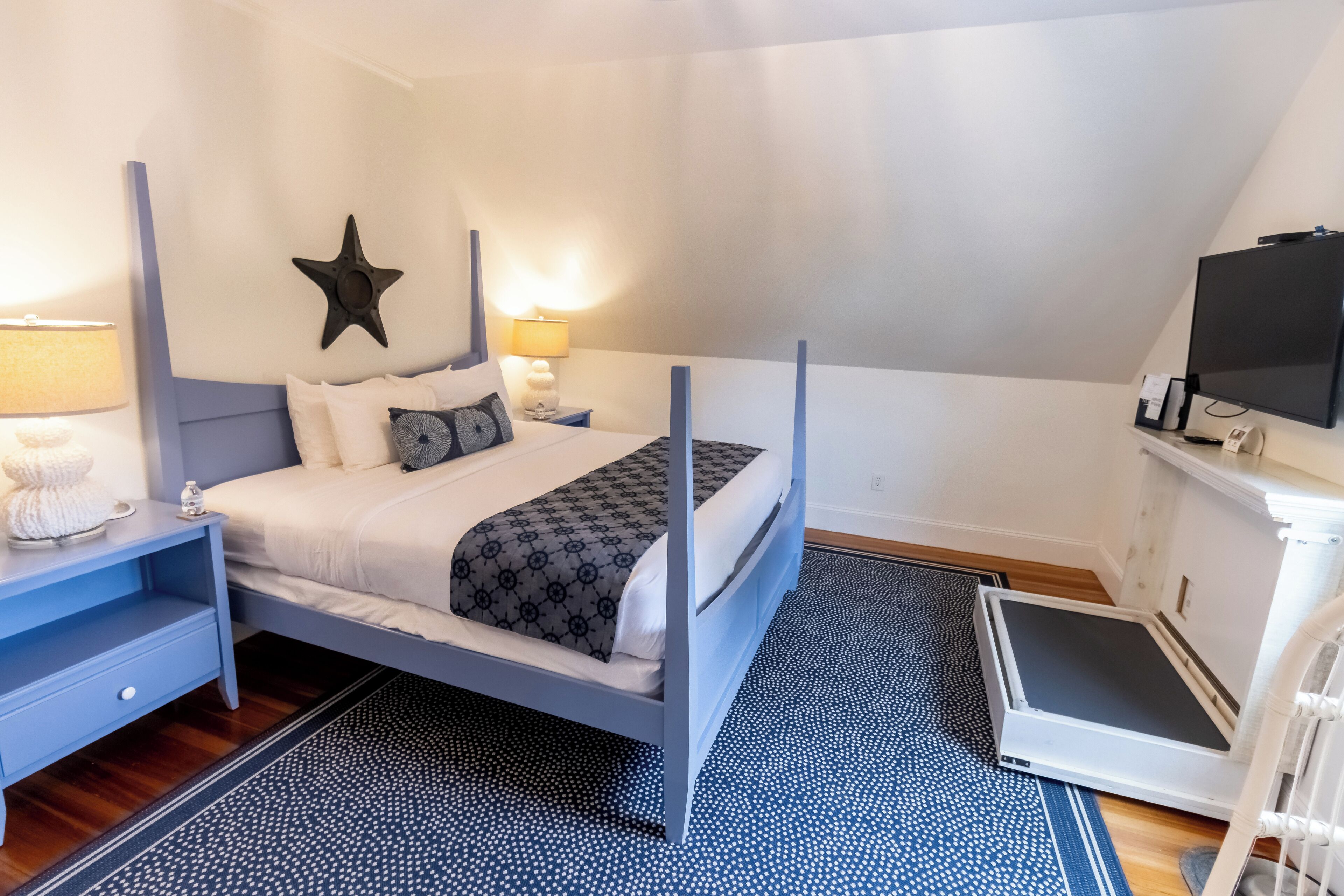 A bedroom with a four-poster bed, a star decoration on the wall, a television, and a desk with a lamp.