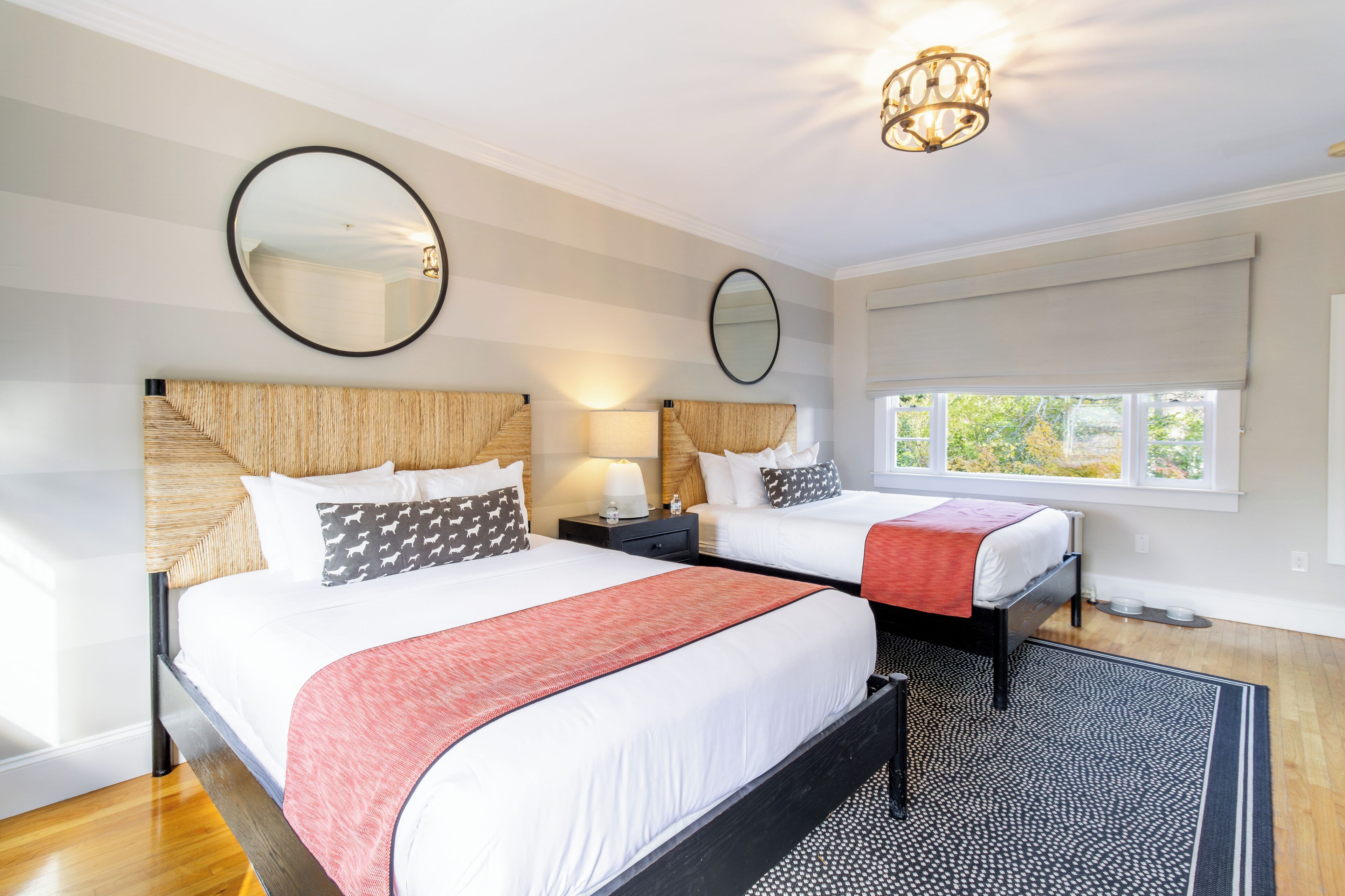 A hotel room with two beds, a large mirror, a chandelier, and a view of the outdoors.