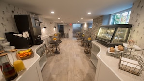 A modern kitchen with a central island, a refrigerator, and a display case with pastries. - Paws on Pelham (Newport)