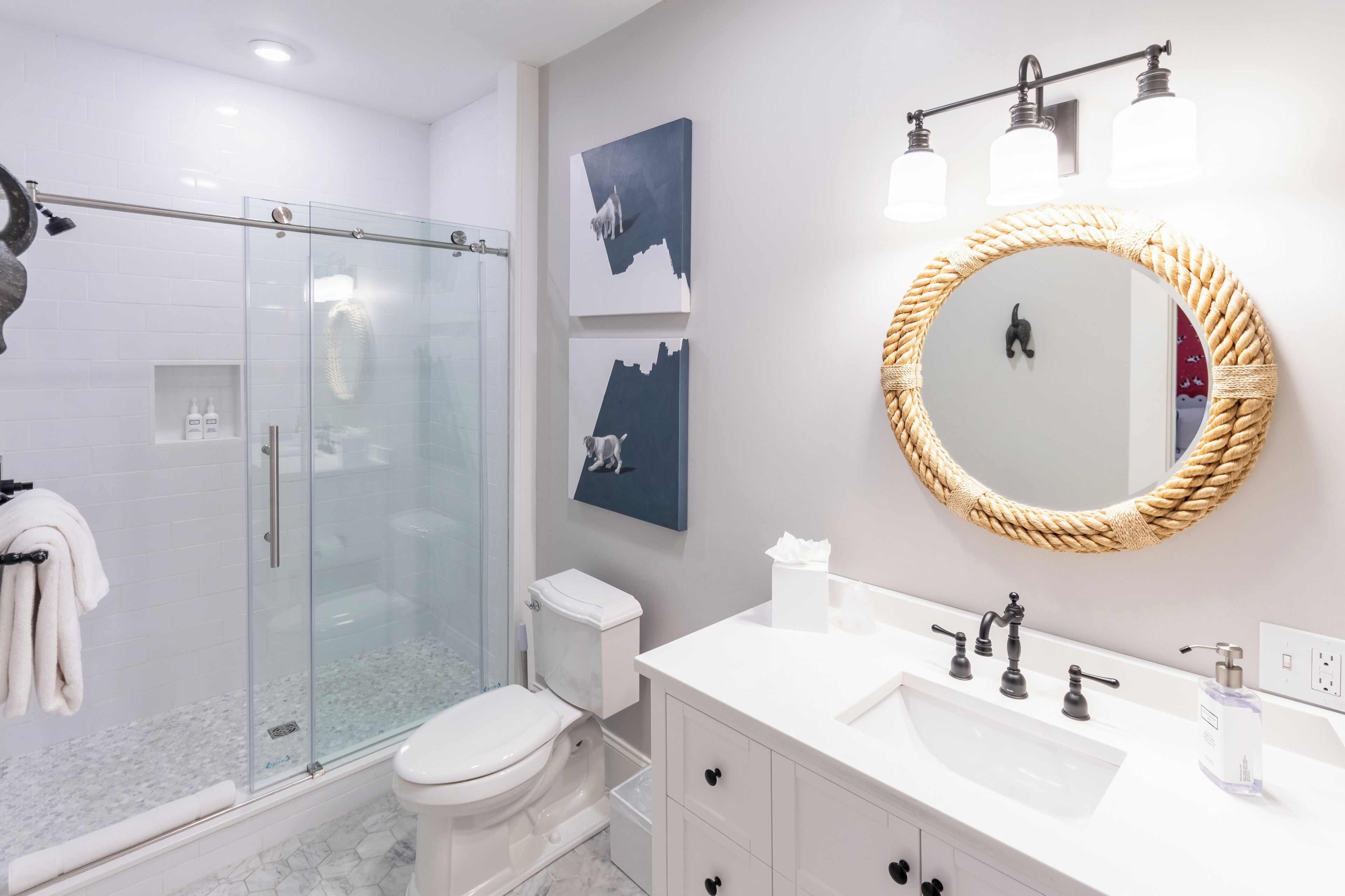 A modern bathroom with a glass-enclosed shower, white fixtures, and artwork on the wall.