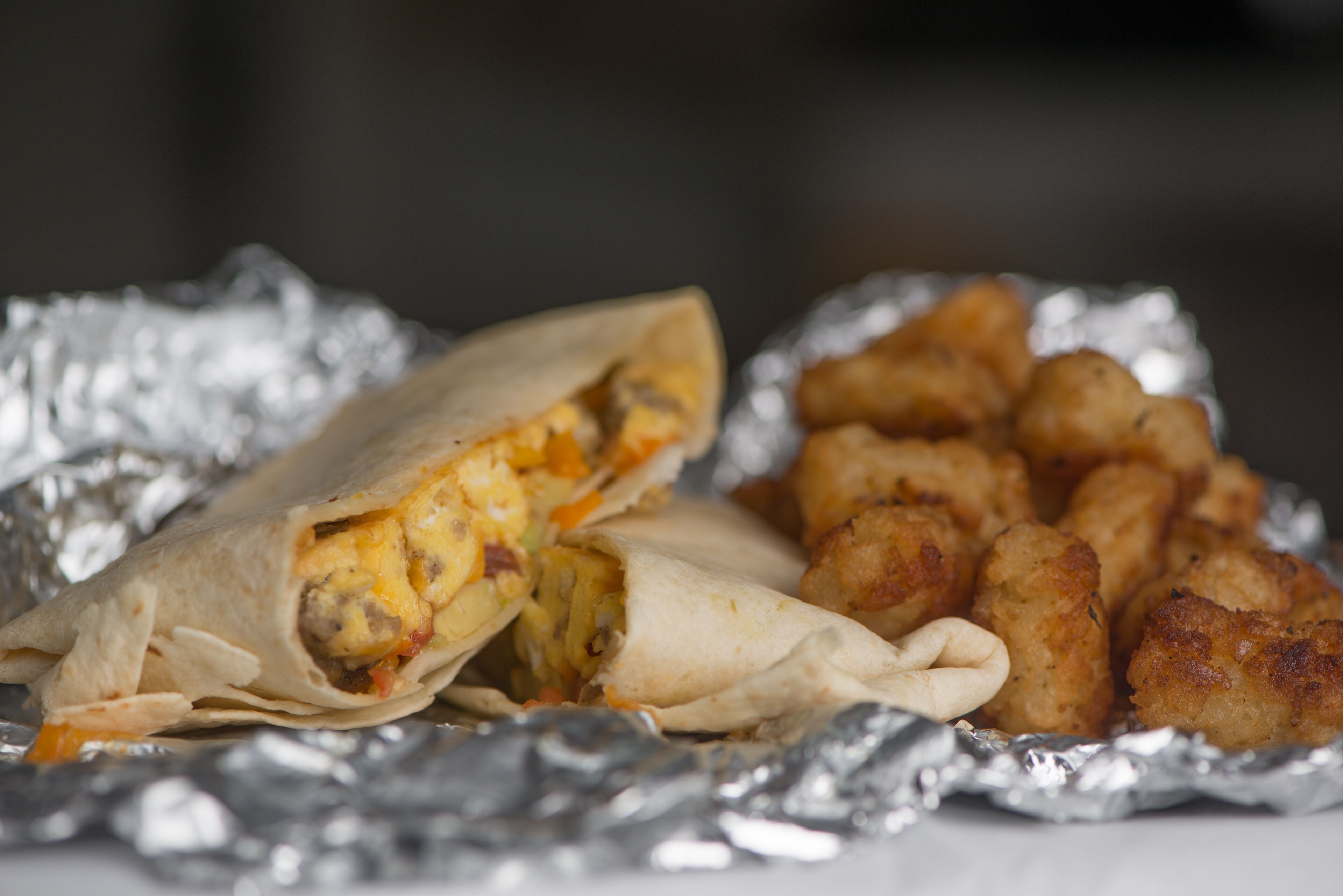 A burrito and tater tots on foil.