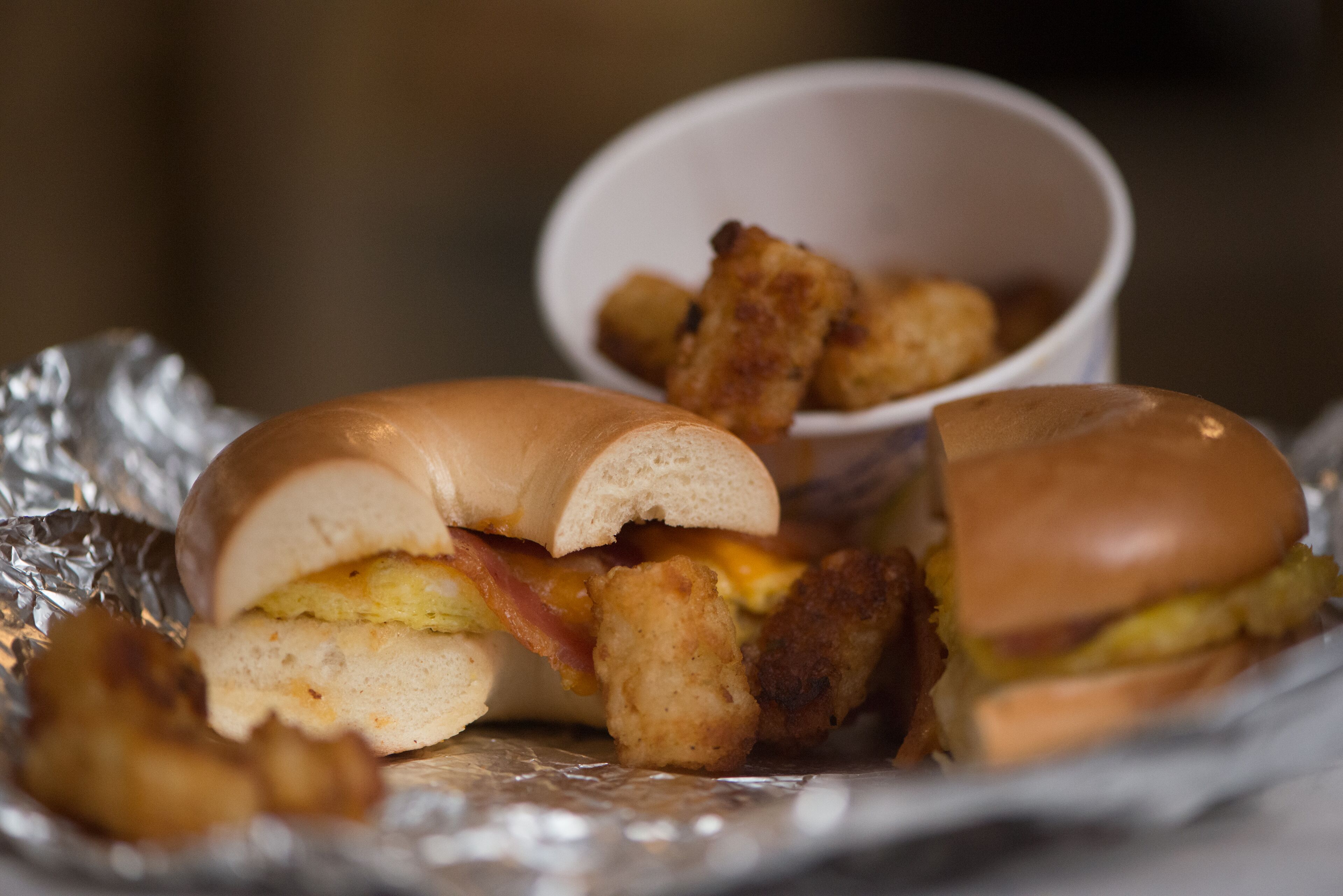 A sandwich with a bun, bacon, and a fried egg, accompanied by tater tots in a small bowl.