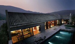A modern house with a swimming pool, large windows, and a tiled roof.