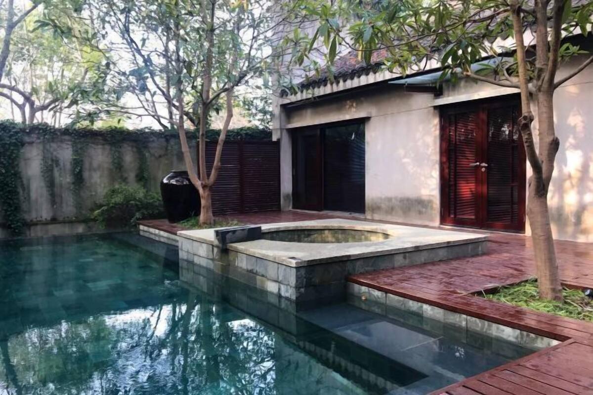 A swimming pool with a stone edge, a wooden deck, and a building with a traditional design.