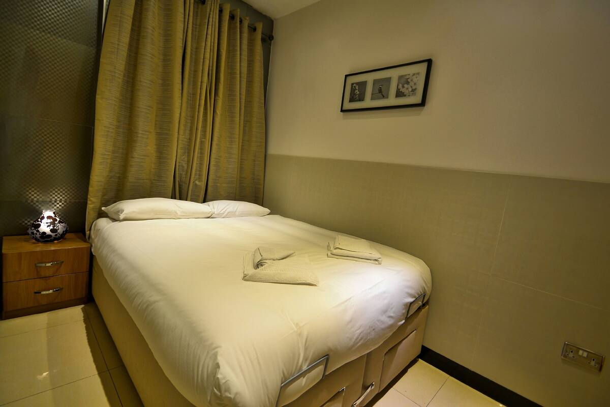 A neatly made bed with white linens, a bedside table with a lamp, and a wall-mounted picture.