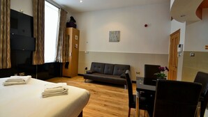 A hotel room with a bed, a sofa, a dining table with chairs, a TV, and a window with curtains.
