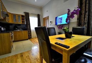Un coin repas avec une table en bois, des chaises noires, une télécommande et un pot d’orchidée.