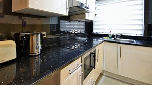 A modern kitchen with black countertops, stainless steel appliances, and white cabinets.