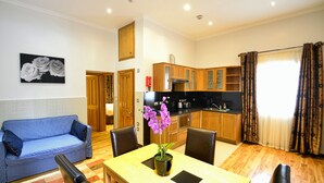 A living room with a blue sofa, a dining table with a potted orchid, wooden cabinets, and a kitchen area.