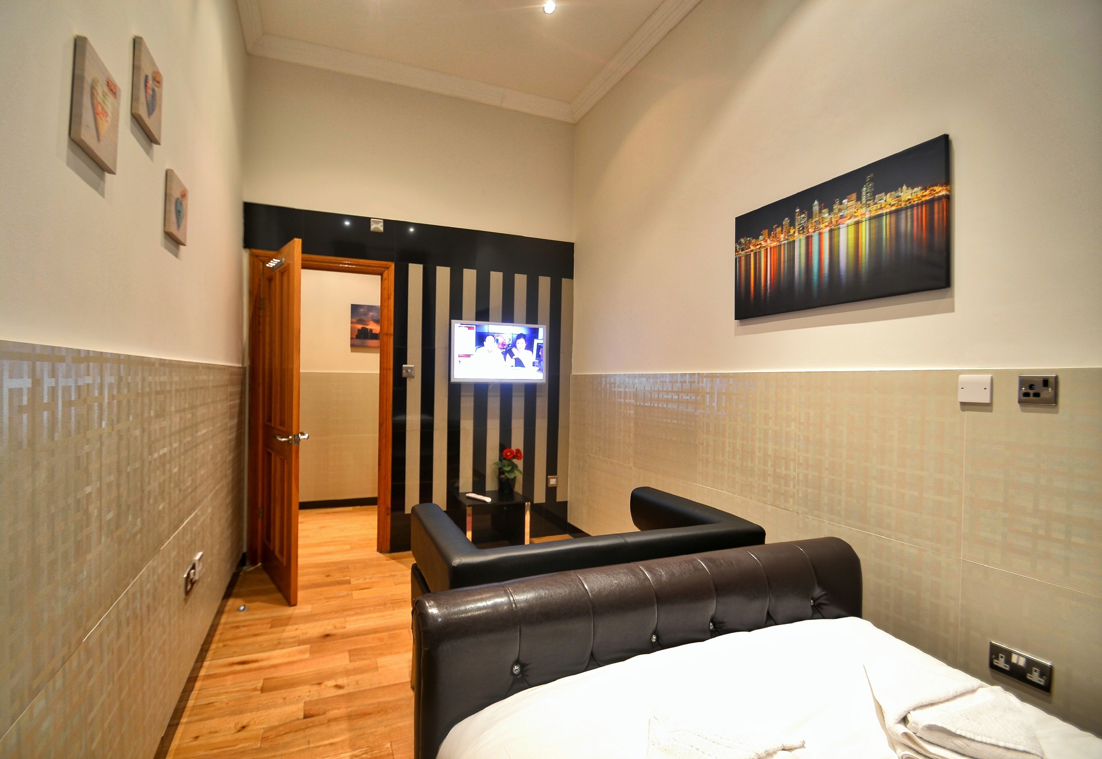 A hotel room with a bed, a TV, a small table with a plant, and a painting on the wall.