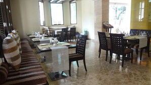 A spacious hotel lobby with a seating area, a dining section, and large windows providing natural light. - Ascot Hotel (Mumbai)