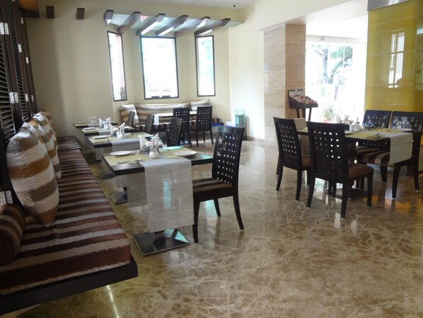 Un vestíbulo de hotel espacioso con zona de estar, área de comedor y grandes ventanales que dejan entrar luz natural.