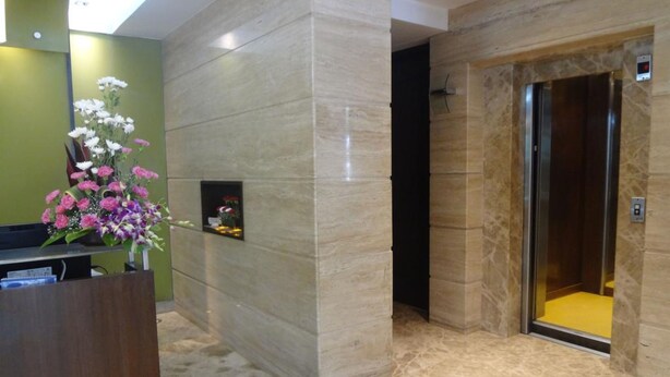 A reception area with a marble floor, a reception desk, a flower arrangement, and an elevator. - Ascot Hotel (Mumbai)