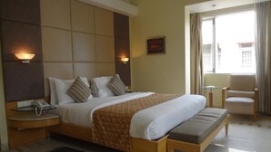 A hotel room with a large bed, bedside tables, a desk, a chair, and a window with curtains. - Ascot Hotel (Mumbai)