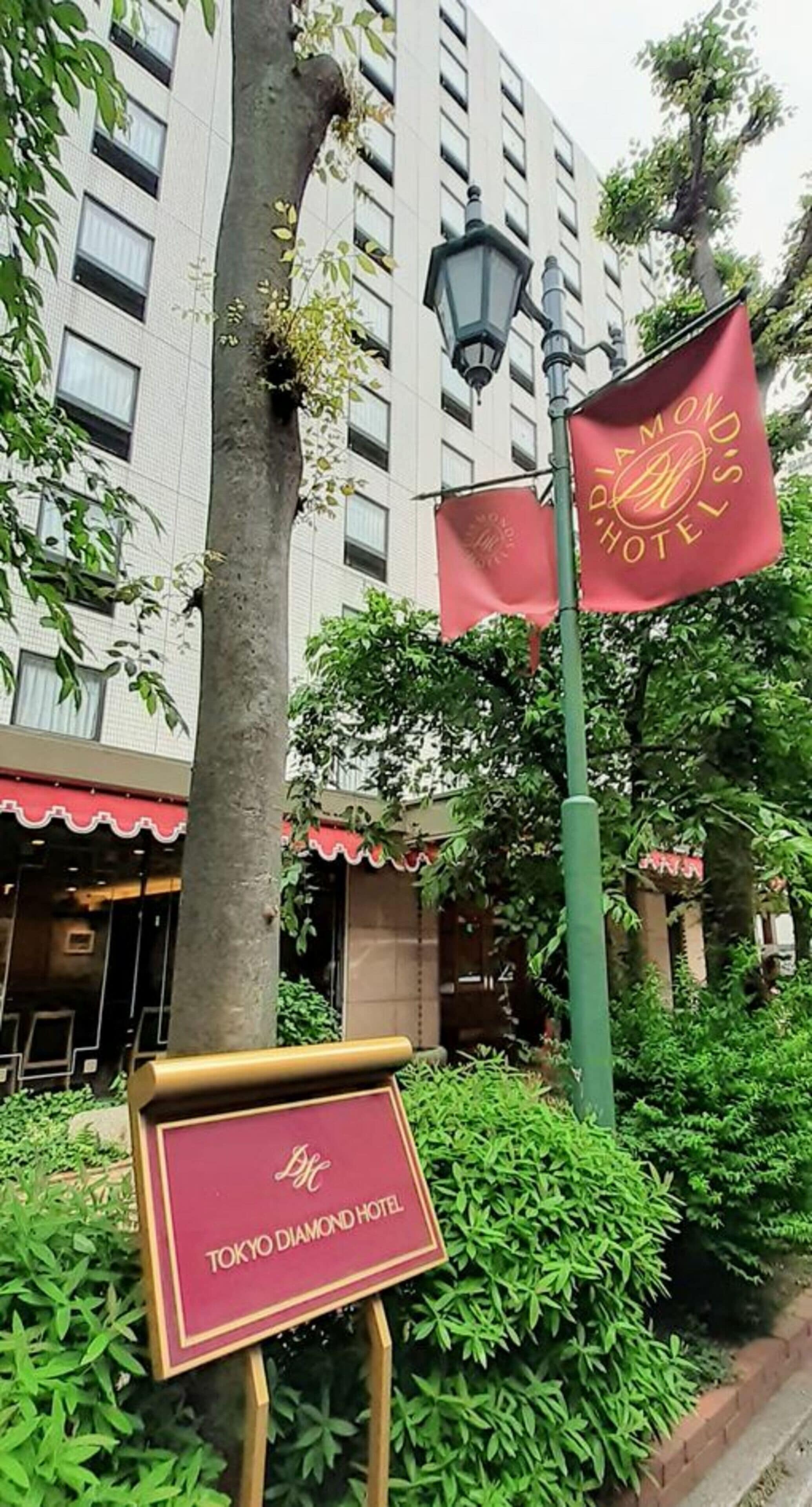 Segnale per l'Hotel Tokyo Diamond con motivo rosso e dorato, un lampione e un edificio con tenda rossa sullo sfondo.
