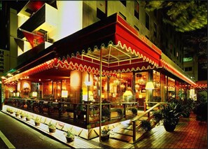 A brightly lit outdoor restaurant with a red awning and outdoor seating.