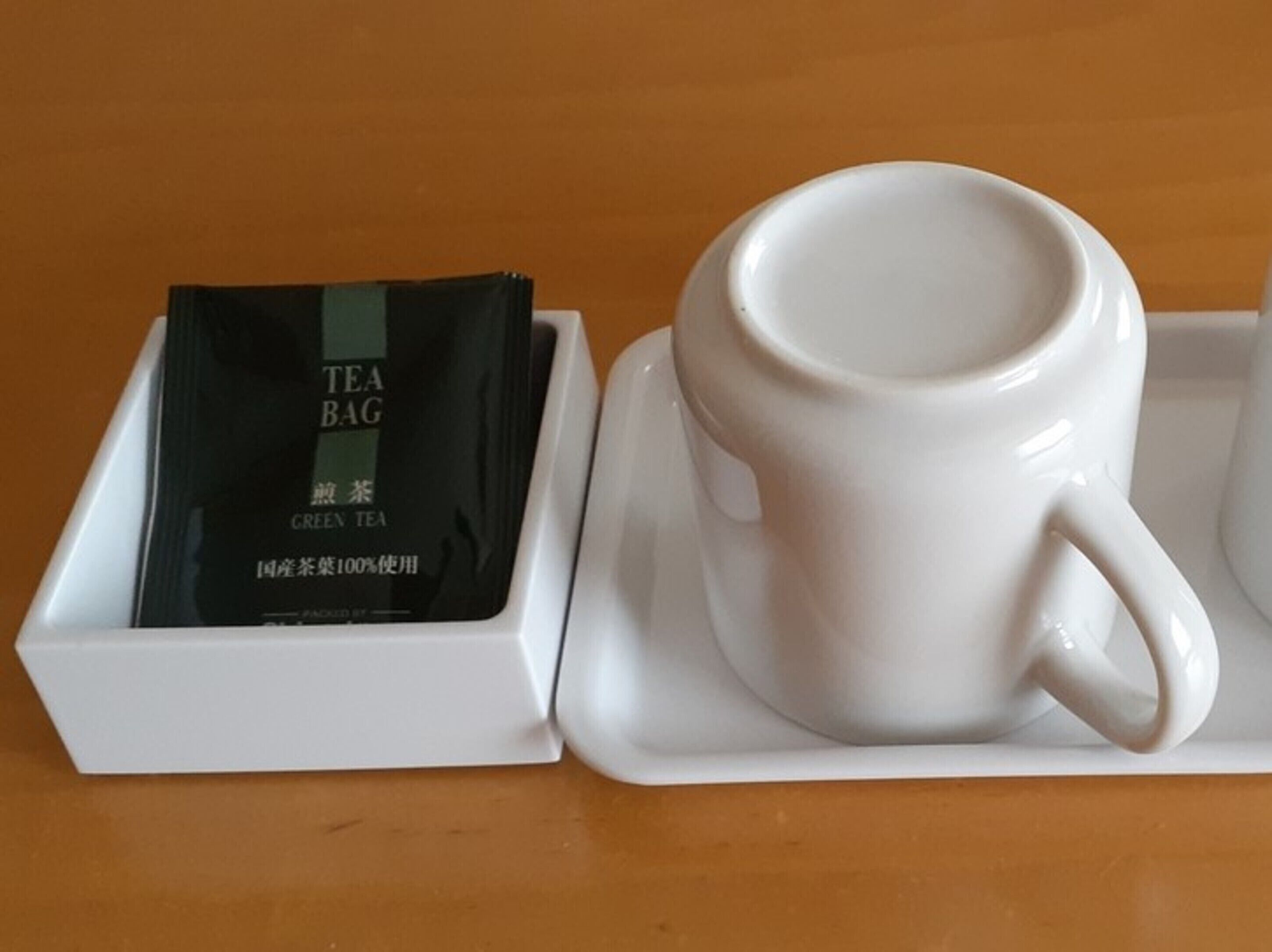 A white ceramic mug on a white tray, next to a white box containing a black tea bag labeled "GREEN TEA".