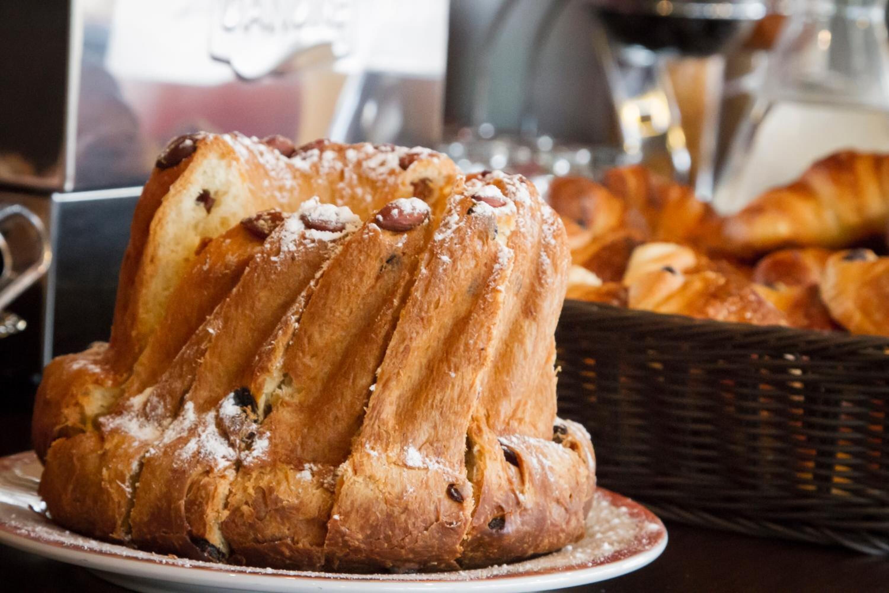 A loaf of bread on a plate with a basket of croissants in the background.