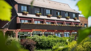 Un edificio de varios pisos con techo inclinado, ventanas grandes y macetas con flores en los balcones.