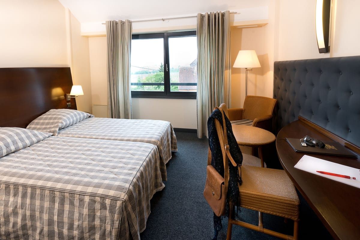 A hotel room with two beds, a desk with a chair, a laptop, and a lamp.