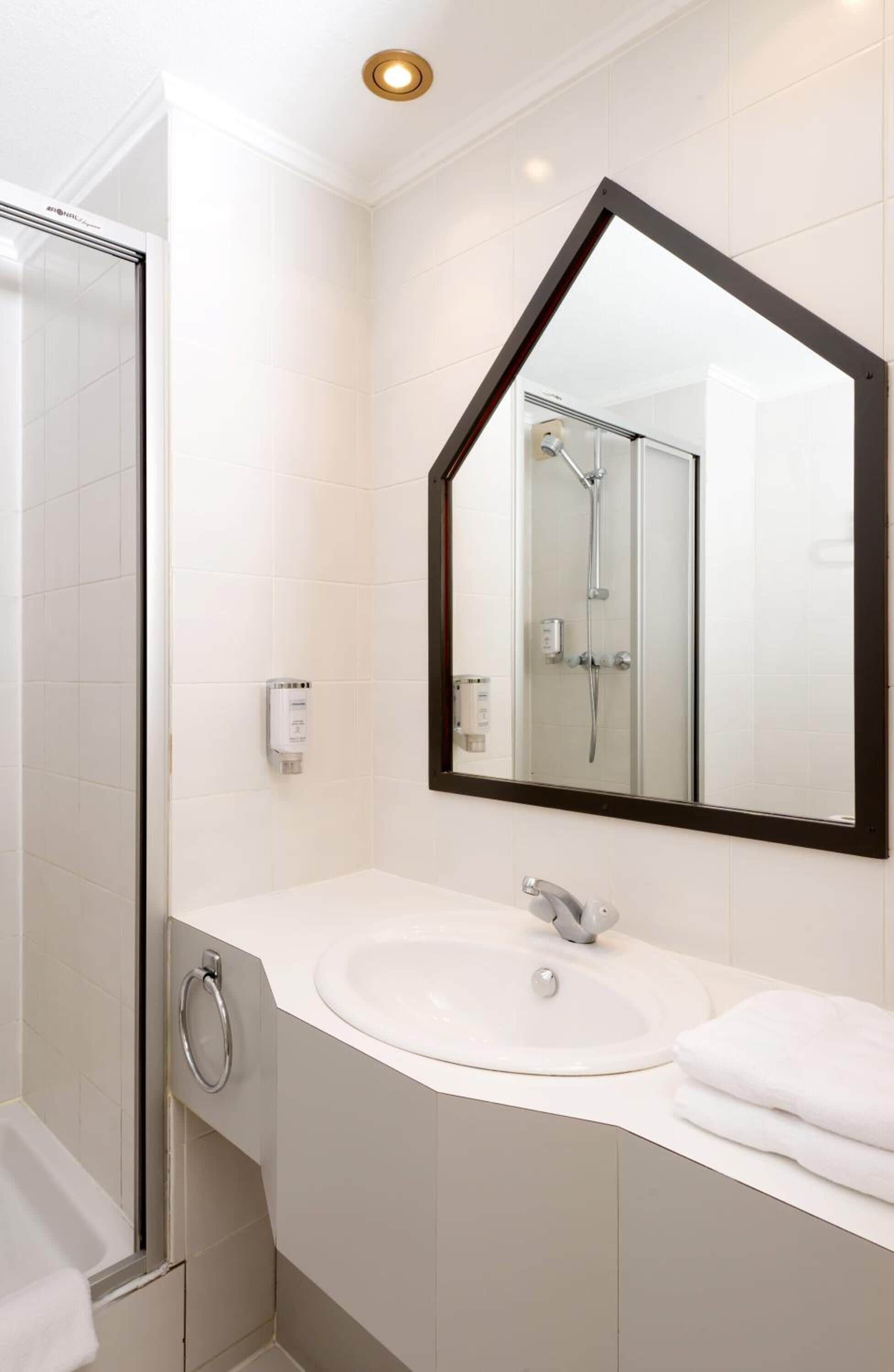 A modern bathroom with a white sink, a large mirror, and a glass shower enclosure.