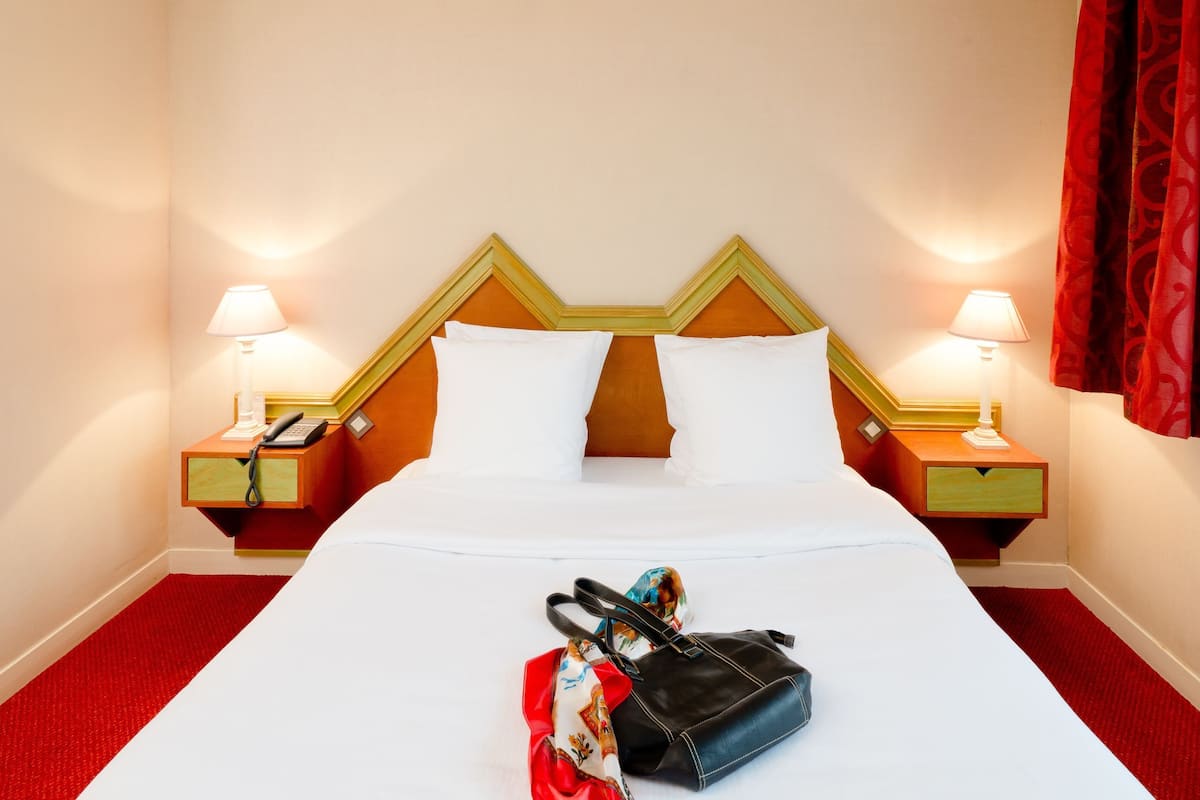 A hotel room with a bed, two bedside tables with lamps, a telephone, and a red curtain.