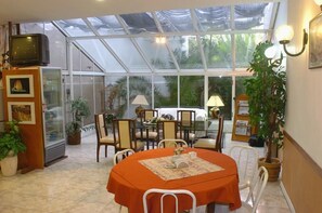 Un invernadero con una mesa, sillas, un televisor y plantas en macetas.